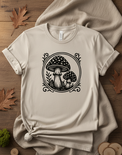 Beige T-Shirt mit schwarzem Pilzmotiv, zwei Pilze in einem dekorativen Kreis, umgeben von Pflanzenmotiven.