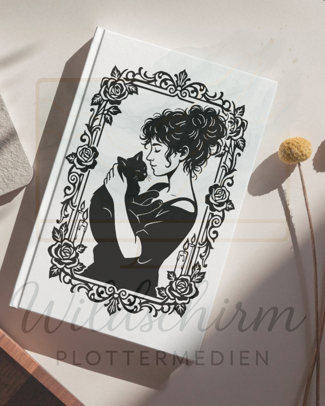 weißes notizbuch auf dem tisch. auf dem einband sieht man eine frau mit einer schwarzen katze 