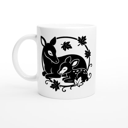 Weiße Tasse mit schwarz-weißer Linienzeichnung von einem liegenden Reh und einem liegenden Rehkitz, umgeben von Blättern.